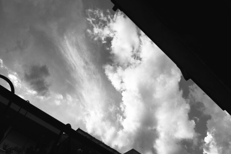Black and white sky with dramatic clouds and building silhouettes.